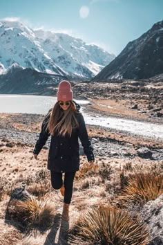 a woman walking through the desert with mountains in the background and snow on the ground