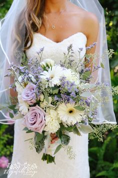 a bride holding a bouquet of white and purple flowers in front of her wedding dress