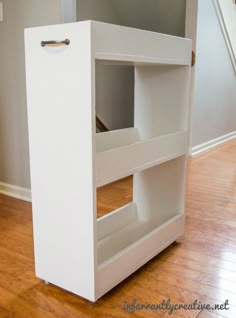 an empty white shelf in the middle of a room with wood flooring and stairs