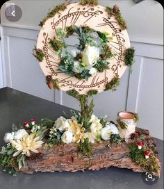 a wooden table topped with flowers and greenery next to a clock on top of a piece of wood