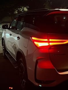 the tail lights of a white suv parked in a parking lot at night with trees behind it