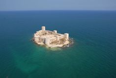 an island in the middle of the ocean with two towers on each side and water around it