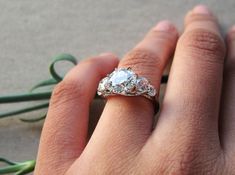 a person's hand with a ring on it and flowers in the foreground