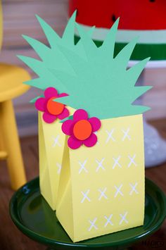 a paper bag with flowers in it sitting on a table next to a cake that is shaped like a pineapple