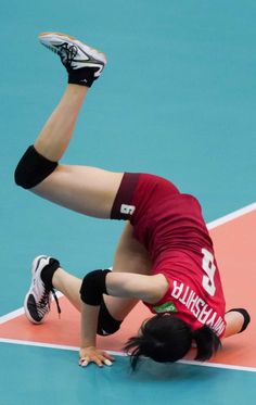 a female volleyball player is falling to the ground with her leg in the air as she dives for the ball