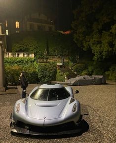 a silver sports car parked in front of a house at night with a man standing next to it