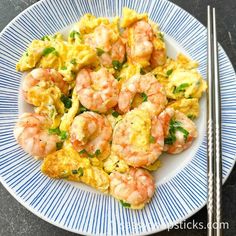 shrimp and scrambled eggs on a blue and white plate with chopsticks next to it