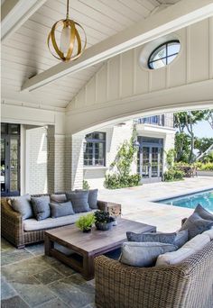 an outdoor living area with couches and tables next to a swimming pool in the background