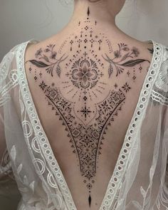 the back of a woman's neck with an intricate tattoo design on her chest