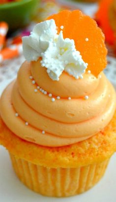 a cupcake with orange frosting and white sprinkles on top is sitting on a table