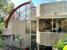 a circular building with many windows and plants in the foreground, surrounded by greenery