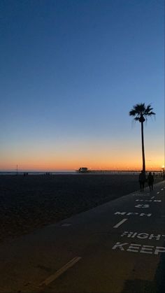 people walking on the beach at sunset with palm trees in the foreground and an ocean pier in the background