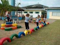 children playing in an outdoor play area with colorful plastic tires on the ground and people standing around