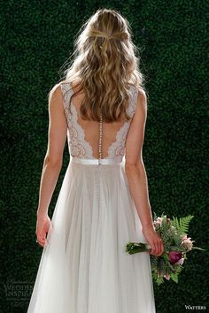 a woman in a white wedding dress holding a bouquet and looking down at the floor