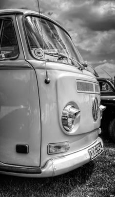 black and white photograph of an old vw bus parked next to another van in the grass