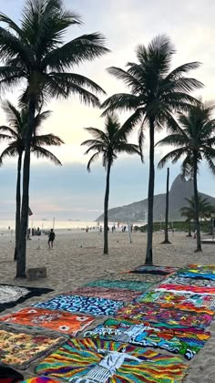 the beach is lined with colorful blankets and palm trees