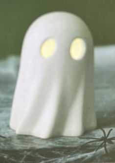 a white ghost with two glowing eyes and a black spider on the ground next to it