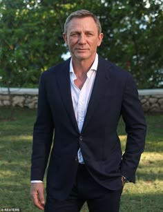 a man in a suit and tie standing on the grass with his hands in his pockets