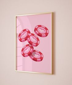 a pink and gold framed art print with red poker chips on the bottom, in front of a light pink wall