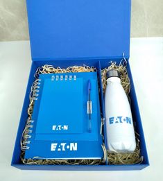 an open blue box containing a notebook, pen and water bottle with straw in it