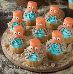 cupcakes with blue frosting and orange decorations on a wooden platter decorated with octopus heads