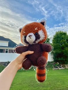 a hand holding a crocheted stuffed animal in front of a house and lawn