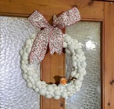 a white wreath with a red bow hanging on the front door and snow balls around it