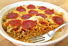 pepperoni pizza on top of noodles in a white bowl with a fork and knife