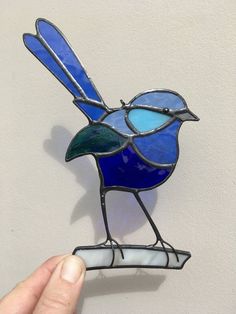 a stained glass blue bird sitting on top of a white wall next to a person's hand