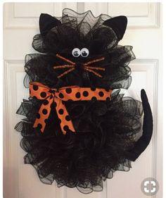 a black cat wreath with orange polka dots on it's face and eyes, hanging from the front door