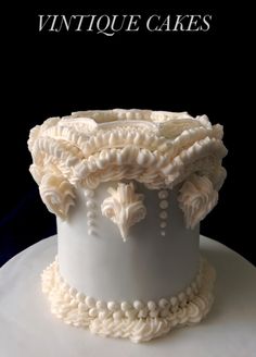 a white cake sitting on top of a plate covered in frosting and beads with the words antique cakes written above it