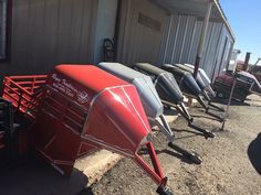 a row of red and black farm equipment parked in front of a building next to a trailer