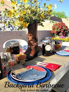 the table is set with plates and flowers in vases, mason jars, jeans napkins, and cowboy boots