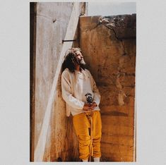 a man with dreadlocks leaning against a wall