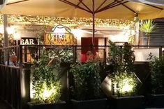 an outdoor restaurant with potted plants on the outside and people sitting at tables under umbrellas