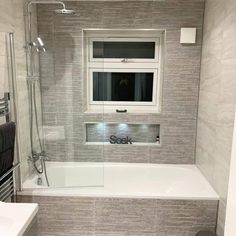 a white bath tub sitting under a window next to a sink and toilet in a bathroom