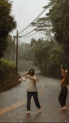 two people standing in the middle of a road with an umbrella over their head and one person holding something up