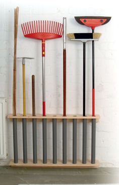 several different types of garden tools are on a shelf next to each other, including rakes and shovels