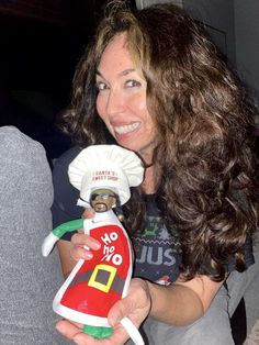 a woman holding a doll with a santa clause on it's head and wearing a hat