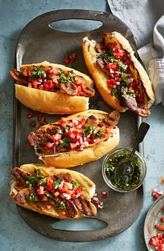 three hot dogs with toppings on a tray next to some condiments and a spoon