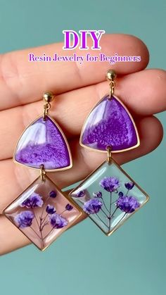 two purple flowers are hanging from small square earrings