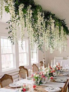 a dining room table with flowers hanging from the ceiling and candles on top of it