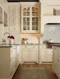 a large kitchen with white cabinets and wooden flooring, along with a rug on the floor