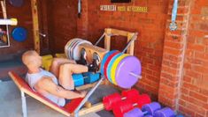 a man laying on top of a wooden bench next to a gym equipment rack and colorful dumbbells