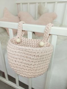 a crocheted basket hanging from the side of a white crib with pink pillows