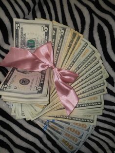 a bunch of money sitting on top of a zebra print blanket with a pink ribbon