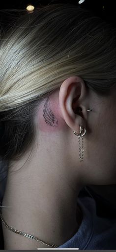 a woman with a tattoo on her left ear and behind the ear is a chain