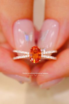 a woman's hand holding an orange diamond ring