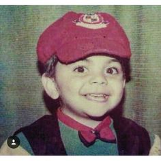 an old photo of a young boy wearing a red hat and vest, smiling at the camera