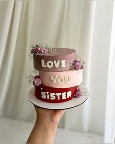 a hand holding a three tiered cake with the words love you sister on it